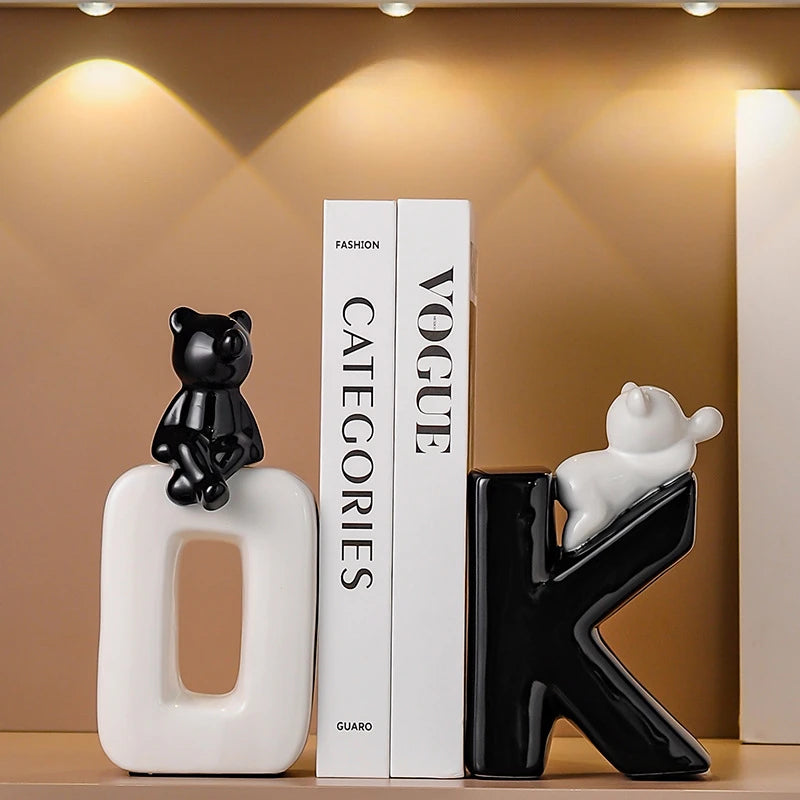 Decorative letter sculptures with cat figures on a shelf against a brown wall.