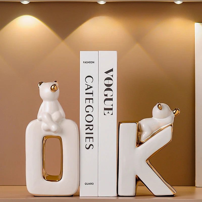 Decorative ceramic letters 'OK' with cat sculptures on a shelf against a brown wall.