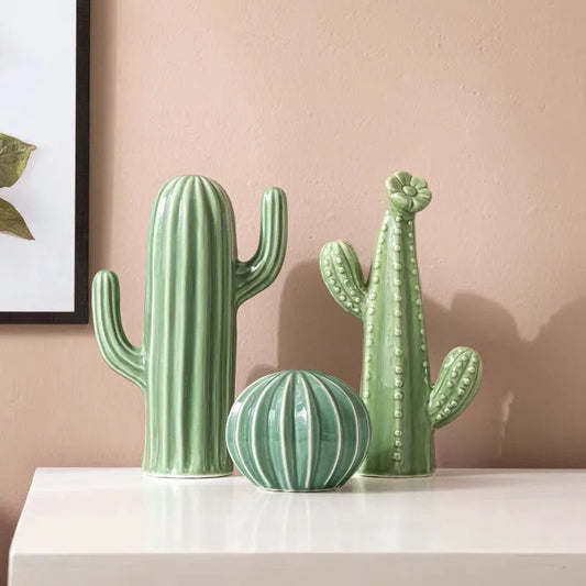 Three green cactus-shaped vases on a white surface with a pink wall background