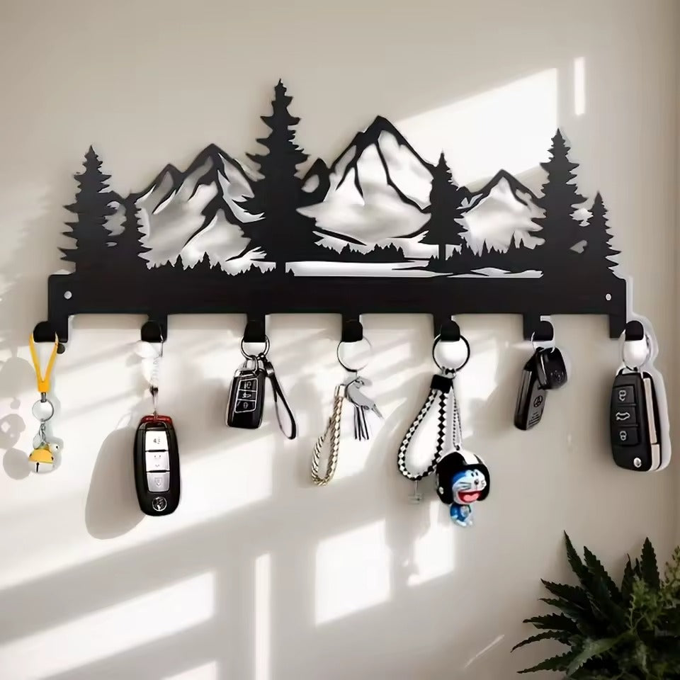 Key holder with mountain design on a wall with keys and items hanging from it.