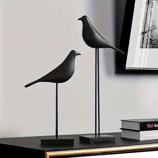 Two black bird sculptures on a shelf with a neutral background