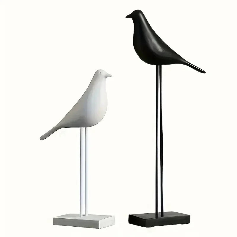 Two bird-shaped sculptures, one white and one black, on stands against a white background.