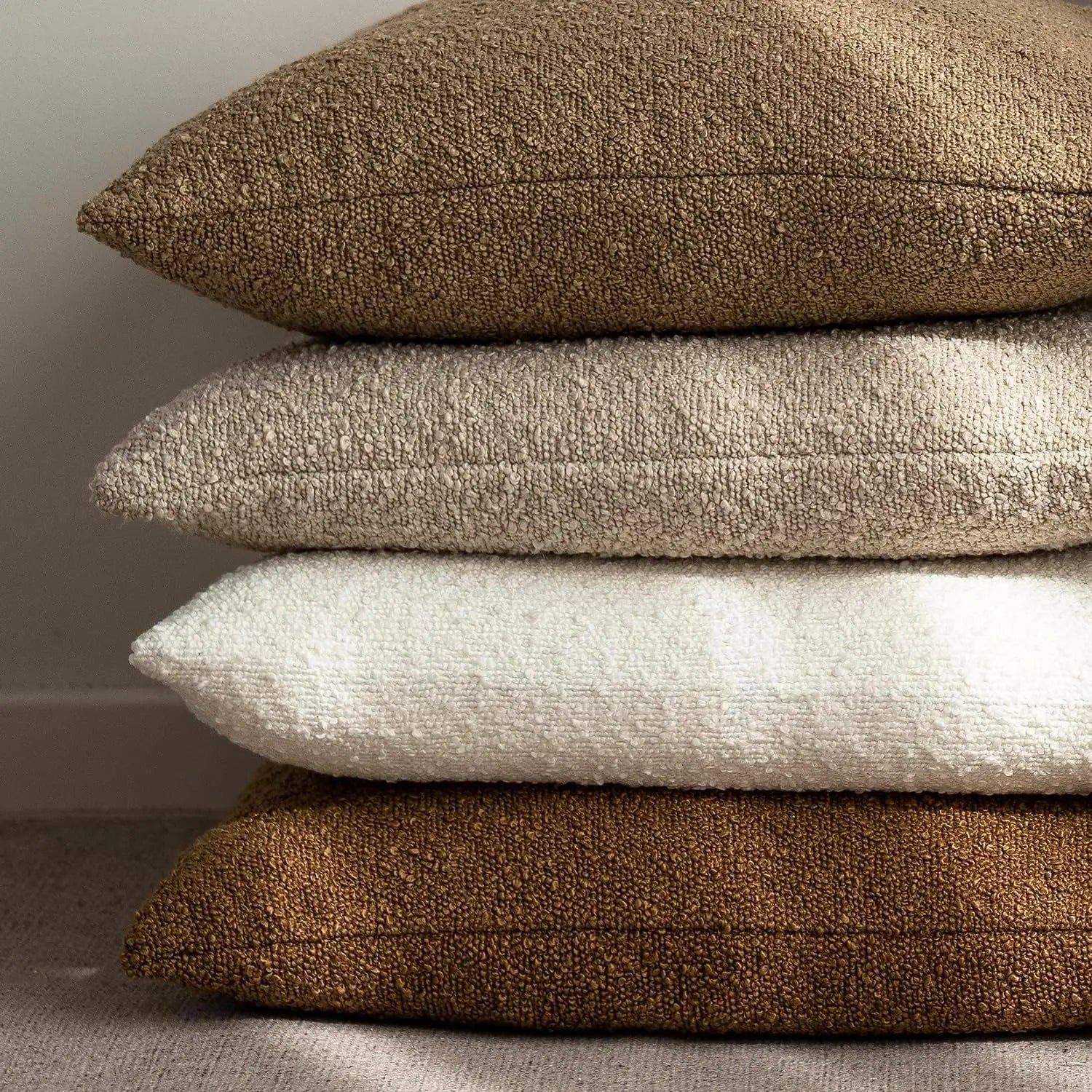 Stack of brown, beige, and white textured pillows on a neutral background