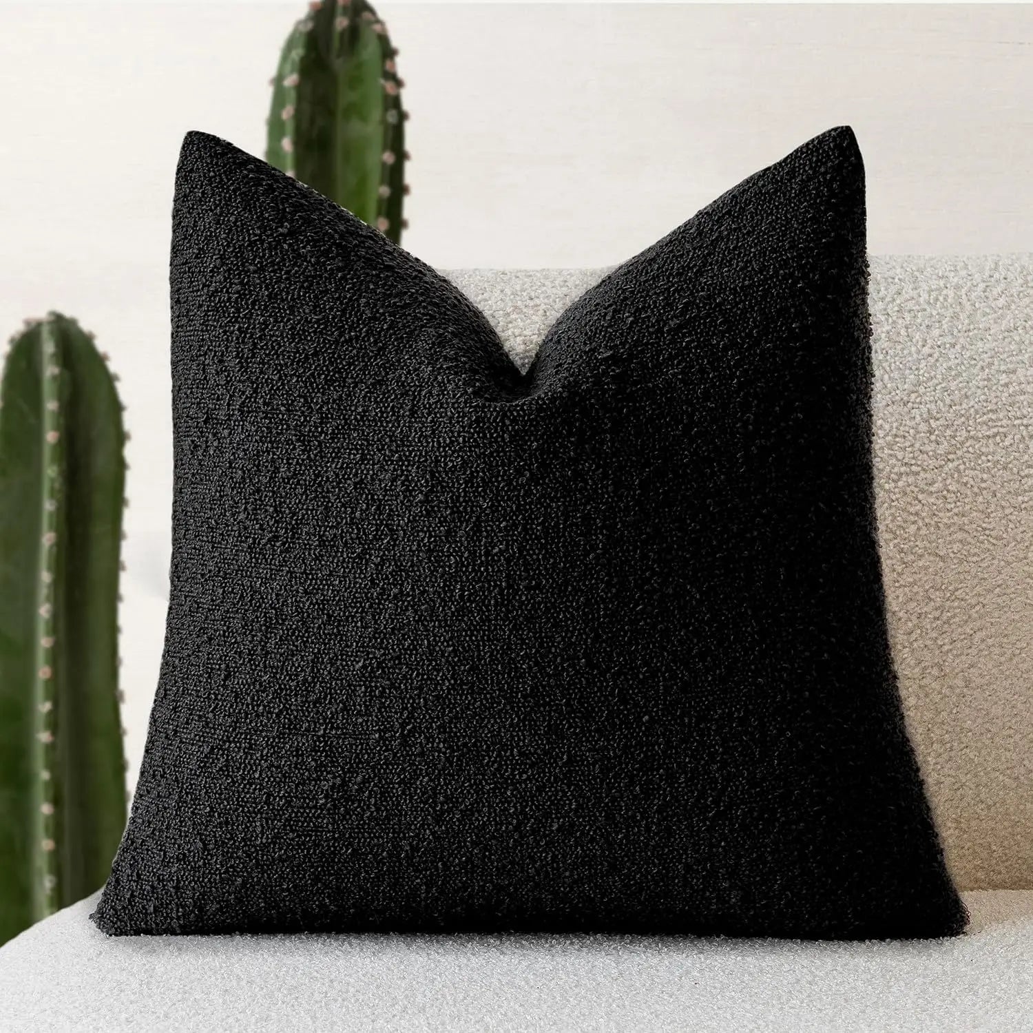 Black textured pillow on a light-colored sofa with a cactus in the background
