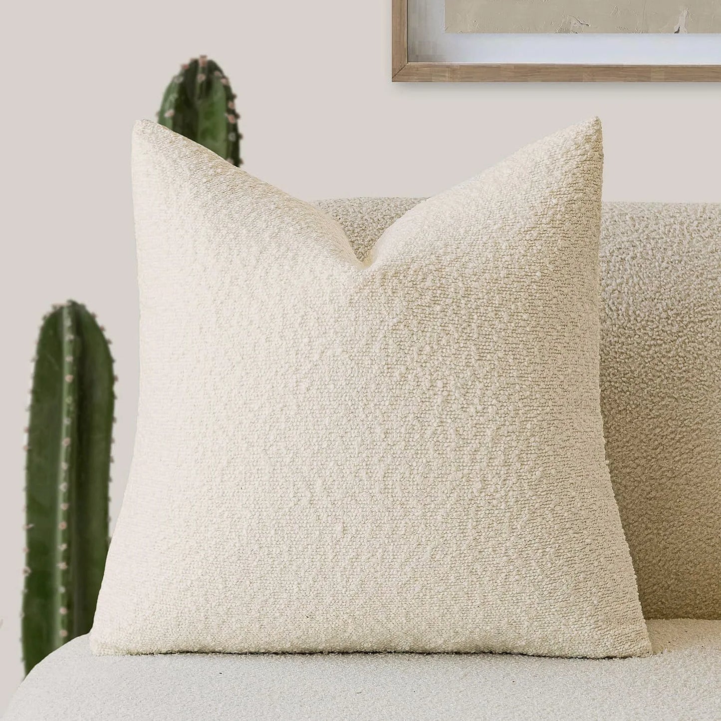 Textured beige pillow on a sofa with a cactus and framed picture in the background