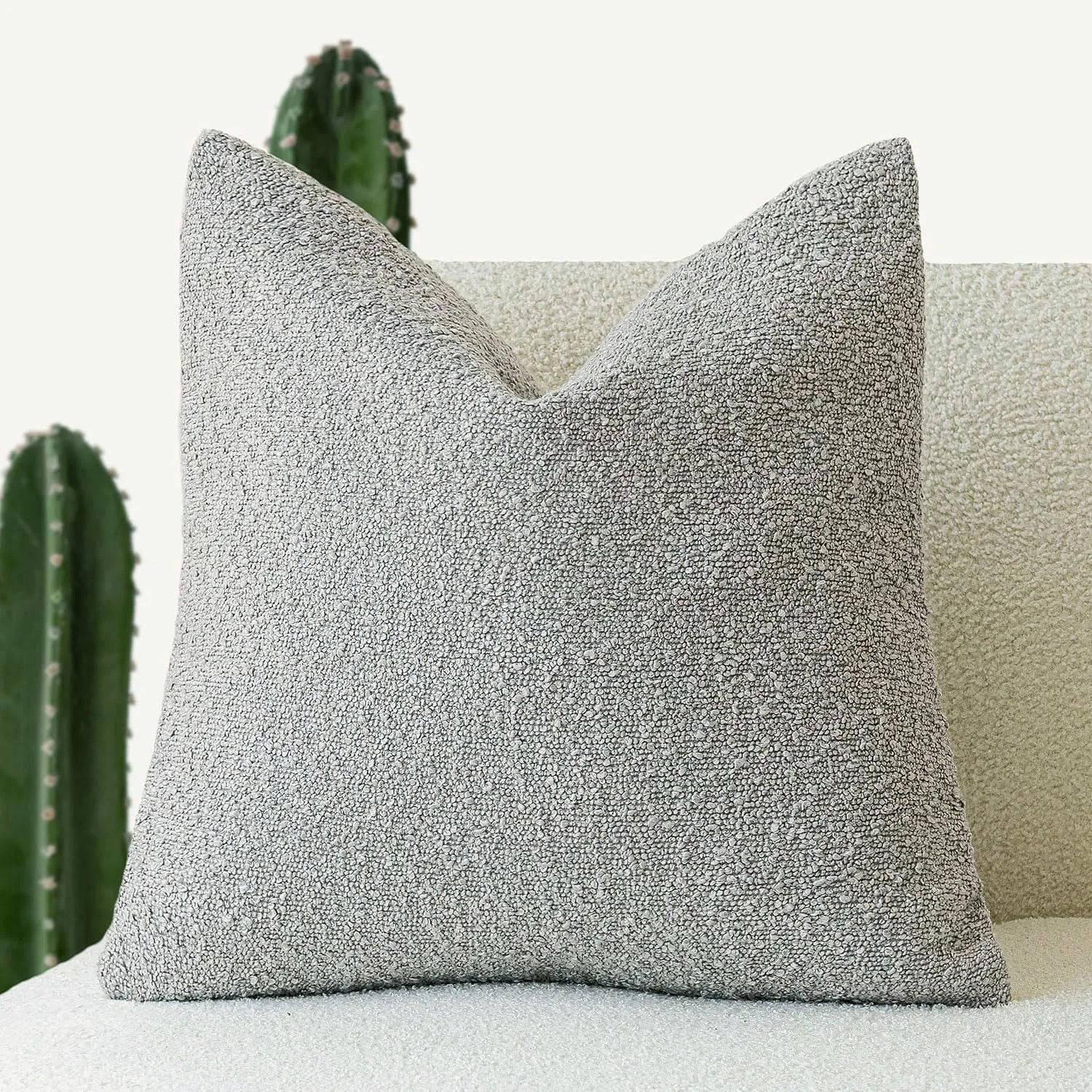 Gray textured pillow on a light-colored sofa with cacti in the background