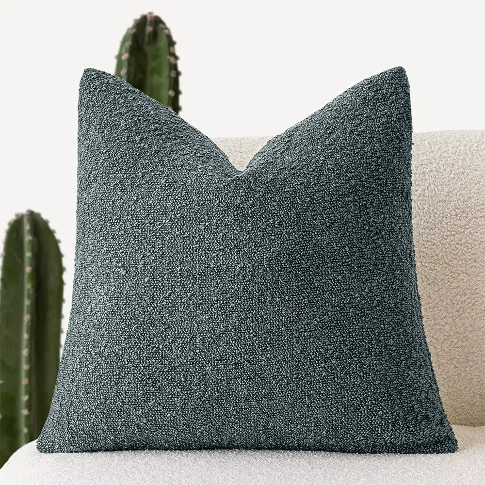 Textured blue-green pillow on a beige sofa with a cactus in the background
