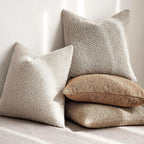 Three textured pillows in beige, brown, and white on a light background