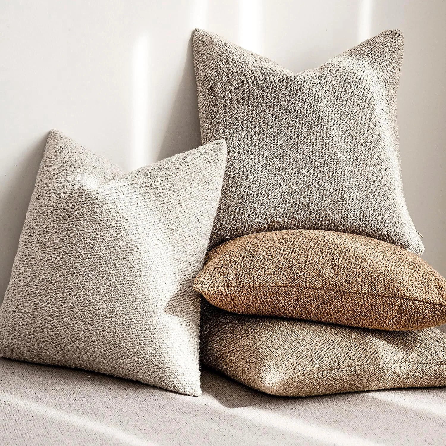 Three textured pillows in beige, brown, and white on a light background