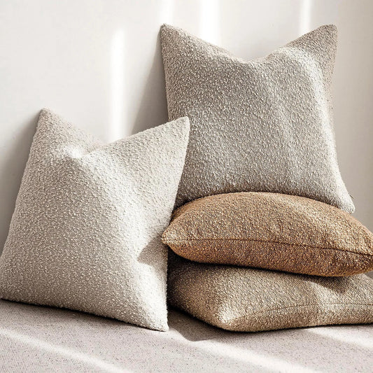 Three textured pillows in beige, brown, and white on a light background