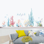 Decorative wall stickers of colorful plants on a white wall above a gray sofa with yellow and white cushions.