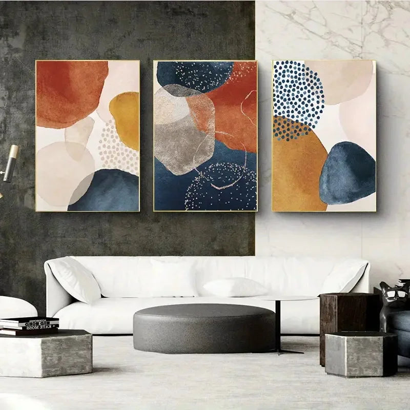 Three abstract art pieces on a wall above a white sofa in a living room.