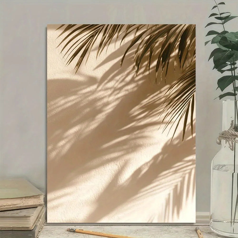 Framed artwork of palm leaves casting shadows on a wall with books and a plant in the foreground.