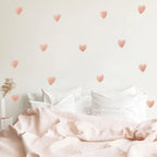 Bed with pink bedding and heart-shaped wall decals on a light background