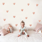 Child sitting on a bed with heart-shaped wall decals and soft pillows.
