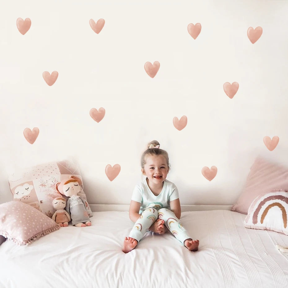 Child sitting on a bed with heart-shaped wall decals and soft pillows.