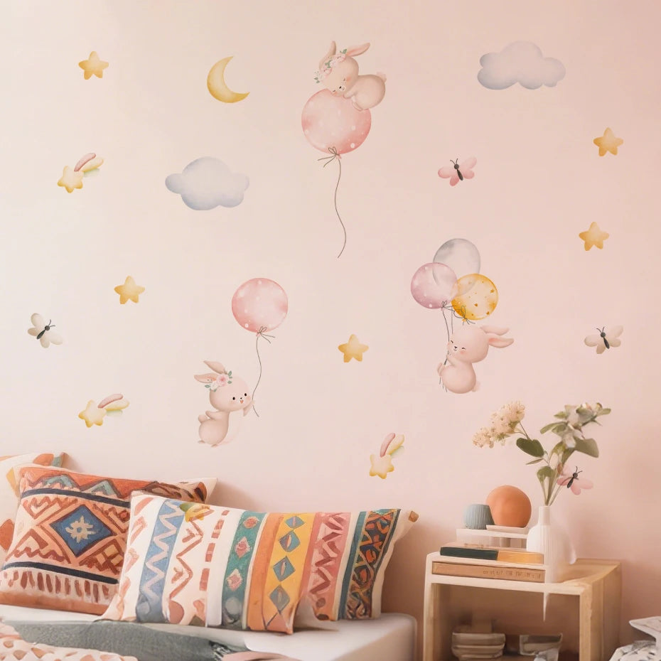 Children's room with decorative wall stickers of rabbits with balloons and clouds on a pink wall.