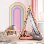 Children's teepee with colorful pom-poms in a room with a rainbow wall mural.
