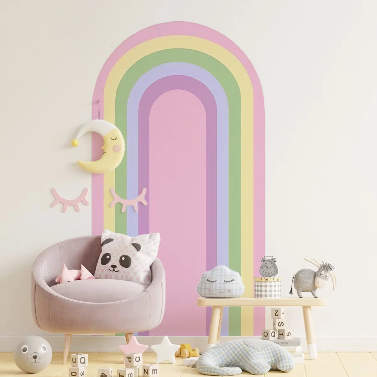 Children's room with pastel rainbow wall decal, soft chair, and toys.