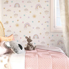Children's room with pastel-colored wallpaper featuring rainbows, stars, and clouds, a pink quilt, and stuffed animals on a bed.