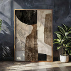 Abstract art piece in a gold frame on a dark wall with a plant to the right.