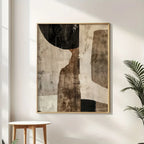Abstract art piece in a gold frame on a wall with a plant and small table.