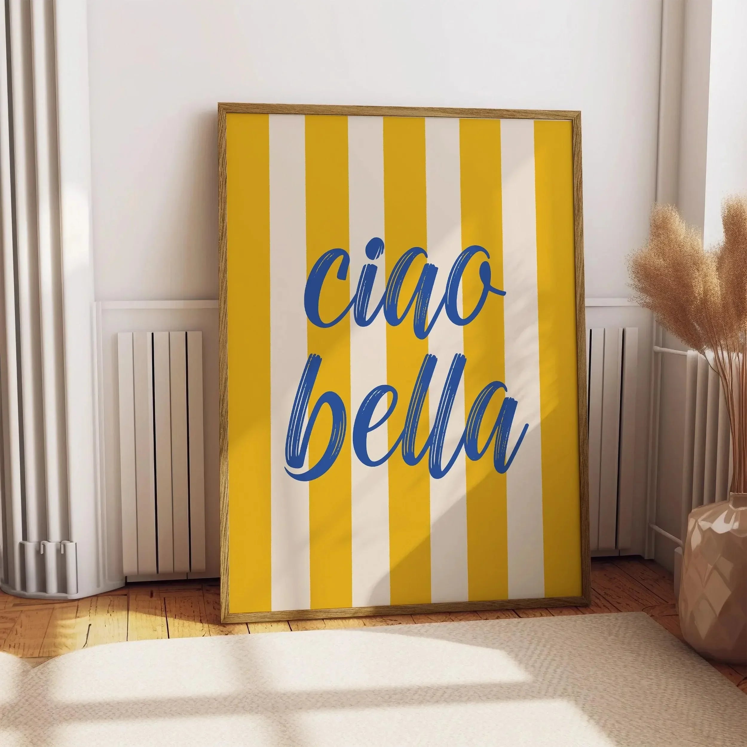 Framed artwork with 'ciao bella' on yellow and white striped background in a room.
