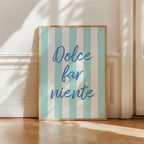 Framed artwork with 'Dolce far niente' text on a striped background, placed indoors.