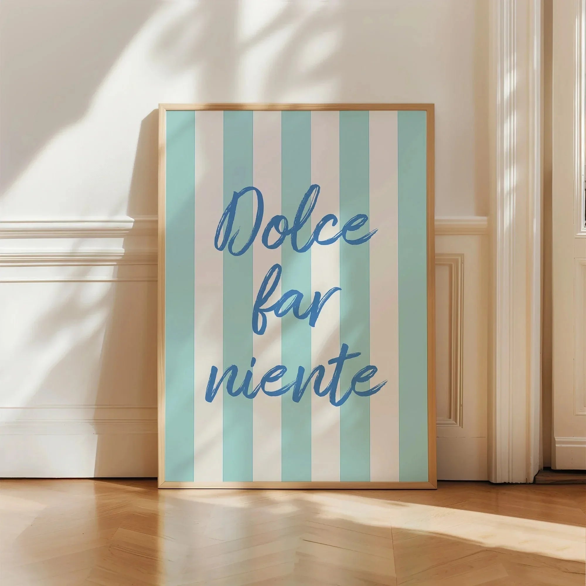 Framed artwork with 'Dolce far niente' text on a striped background, placed indoors.