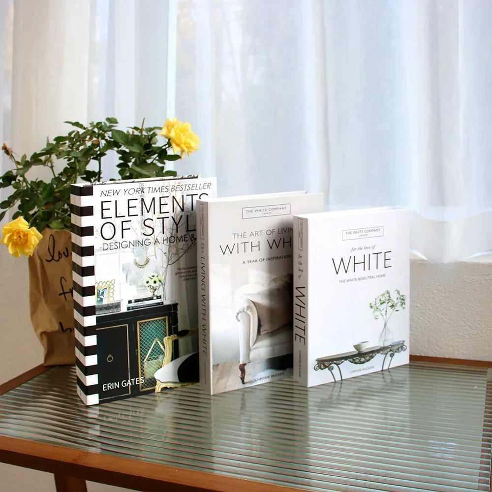 Three books on a glass table with a plant in the background