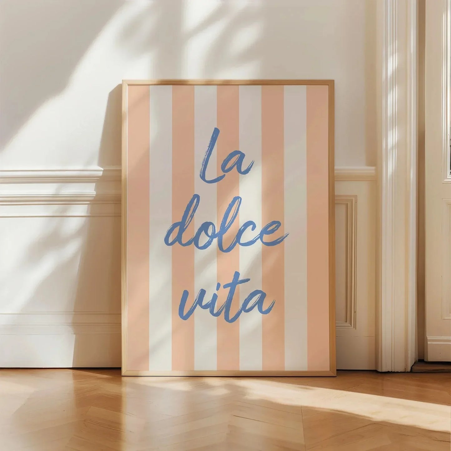 Framed artwork with 'La dolce vita' text on a striped background, placed on a wooden floor.