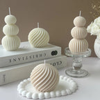 Decorative candles with ribbed texture on a white surface with books and a vase in the background.