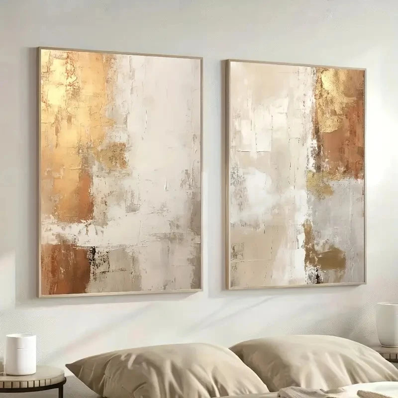 Two abstract art pieces in gold and beige tones on a wall above a bed.