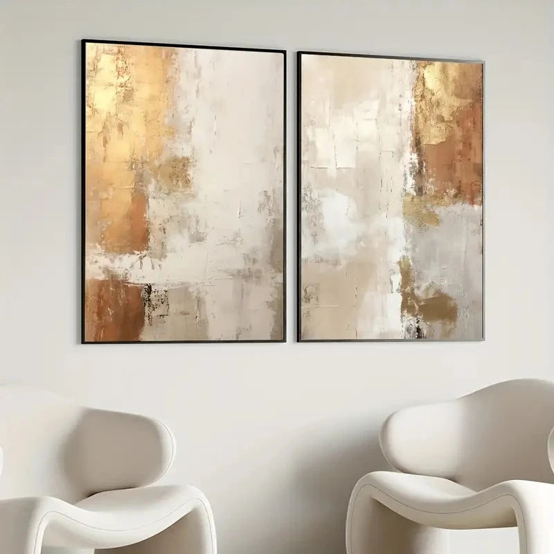 Two abstract art pieces in gold and beige tones on a wall with white chairs.