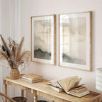 Two framed artworks on a wall above a wooden console table with books and a vase.