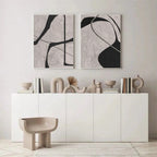 Two abstract black and white paintings above a white cabinet with decorative items.