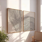 Two abstract wall art pieces with wavy lines on a light wall, with a plant and chair in the foreground.