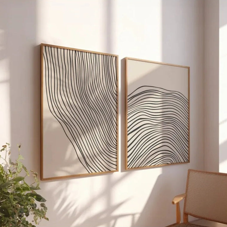 Two abstract wall art pieces with wavy lines on a light wall, with a plant and chair in the foreground.