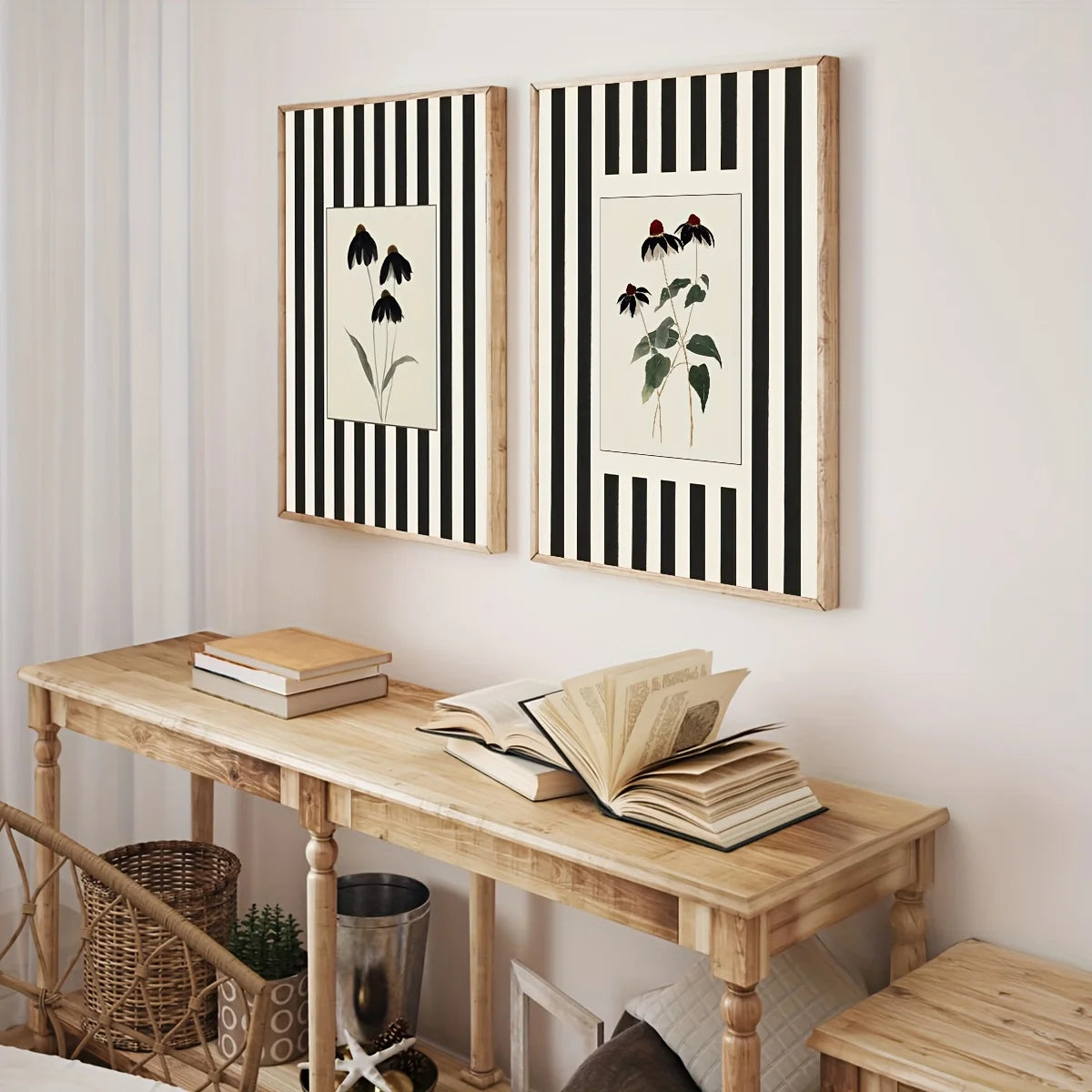 Two framed botanical art prints with black and white vertical stripes hang on a light wall above a wooden console table with books.