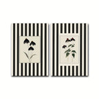 Two vertical canvas wall art prints with black and white vertical stripes, each featuring a central botanical illustration. The left print shows black coneflowers on a cream background, and the right print shows similar flowers with green leaves and red buds on a cream background.