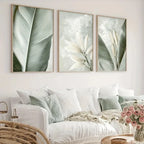 Three framed botanical prints above a white sofa with decorative pillows and flowers.