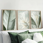 Three framed botanical prints above a bed with green and white bedding.