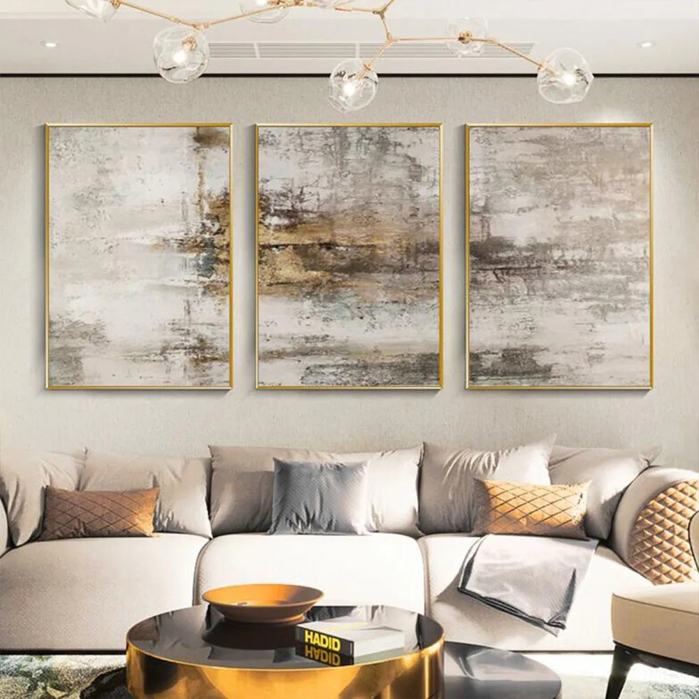 Three-piece abstract wall art set with gold frames hanging above a modern beige sofa in a styled living room.