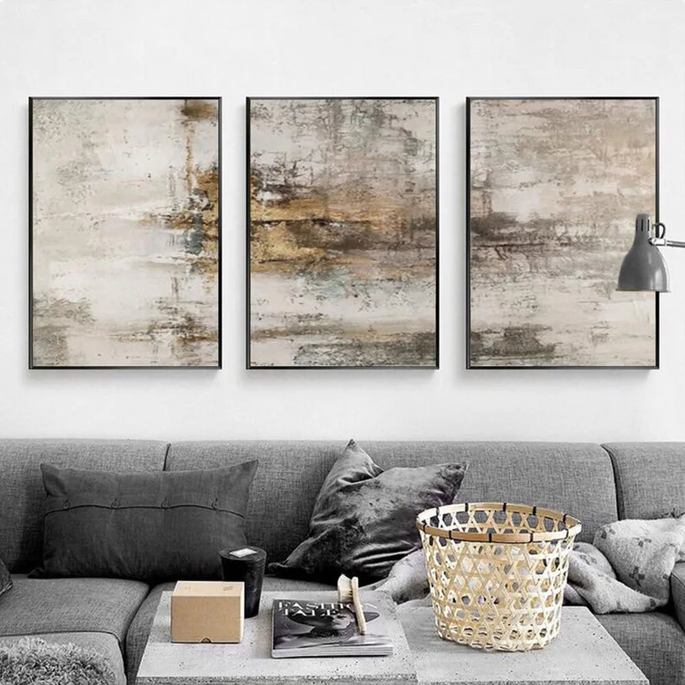 Three-piece framed wall art set with abstract textured designs in beige, gray, and brown tones, displayed above a gray sofa in a modern living room setting.