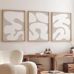 Three abstract wall art pieces in wooden frames on a white wall above a wooden console table.