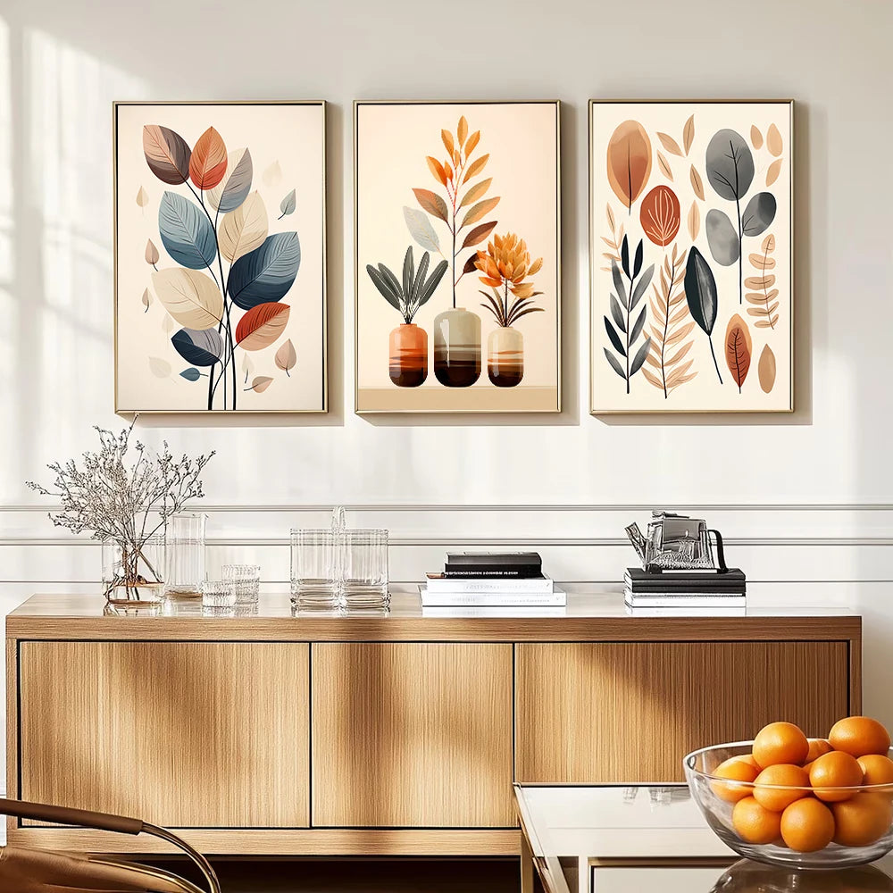 Three framed leaf prints above a wooden cabinet with a bowl of oranges on a glass table.