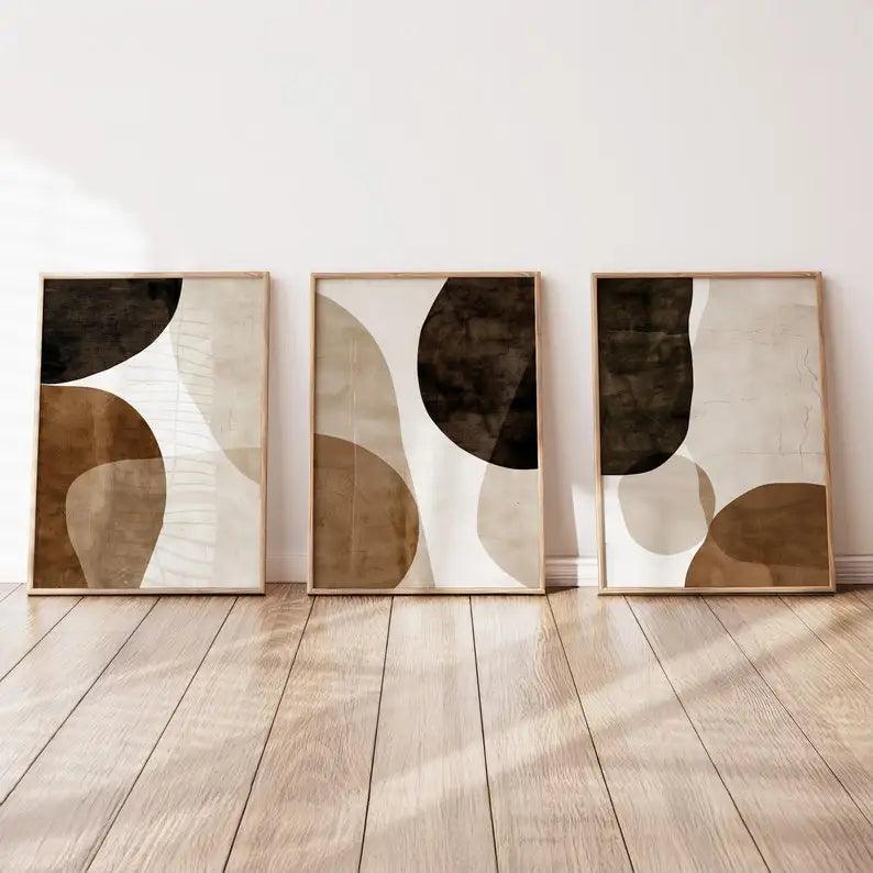 Three abstract art pieces in wooden frames on a white wall with a wooden floor.