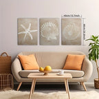 Three wall art pieces with starfish and shell designs above a beige sofa with orange cushions.