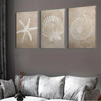 Three wall art pieces with starfish, shell, and spiral design on a gray wall above a sofa.