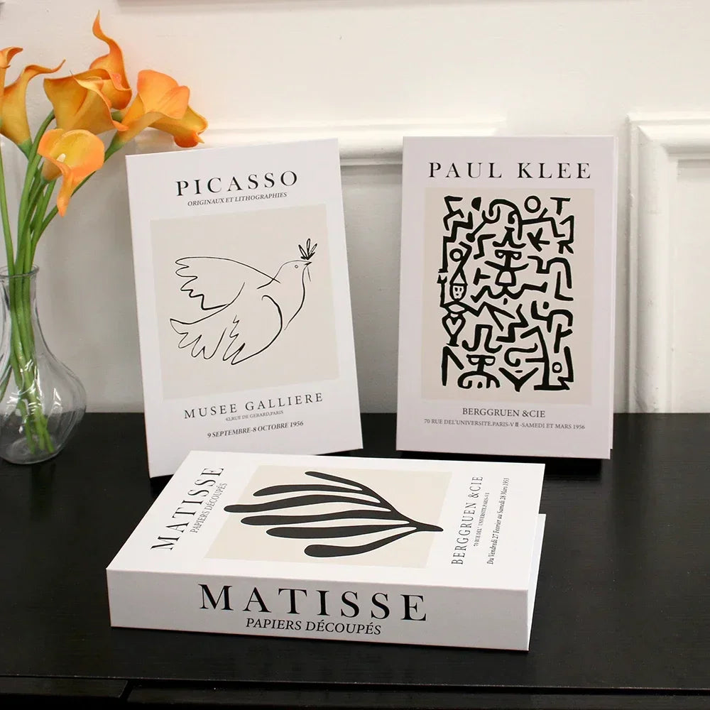 Three art books by Picasso, Matisse, and Paul Klee on a dark surface with flowers in the background.